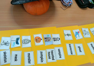 Grupa uczniów pracuje przy stolikach, dopasowując obrazki związane z Halloween do angielskich podpisów.