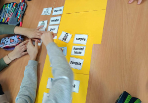 Grupa uczniów pracuje przy stolikach, dopasowując obrazki związane z Halloween do angielskich podpisów.