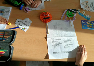 Uczniowie siedzą przy ławkach i wspólnie rozwiązują krzyżówkę z hasłami dotyczącymi Halloween.